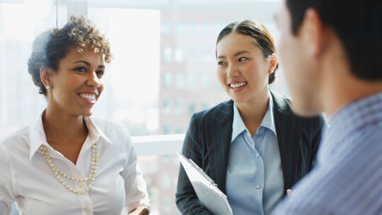 Kollegen unterhalten sich in einem hellen Büro mit großen Fenstern und Stadtblick.