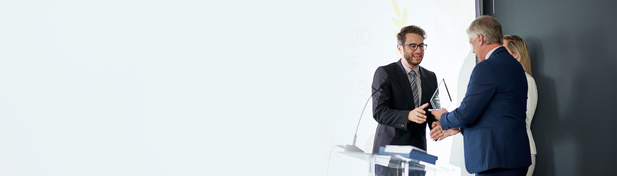 Zwei Menschen erhalten eine Auszeichnung von einem Redner auf dem Podium
