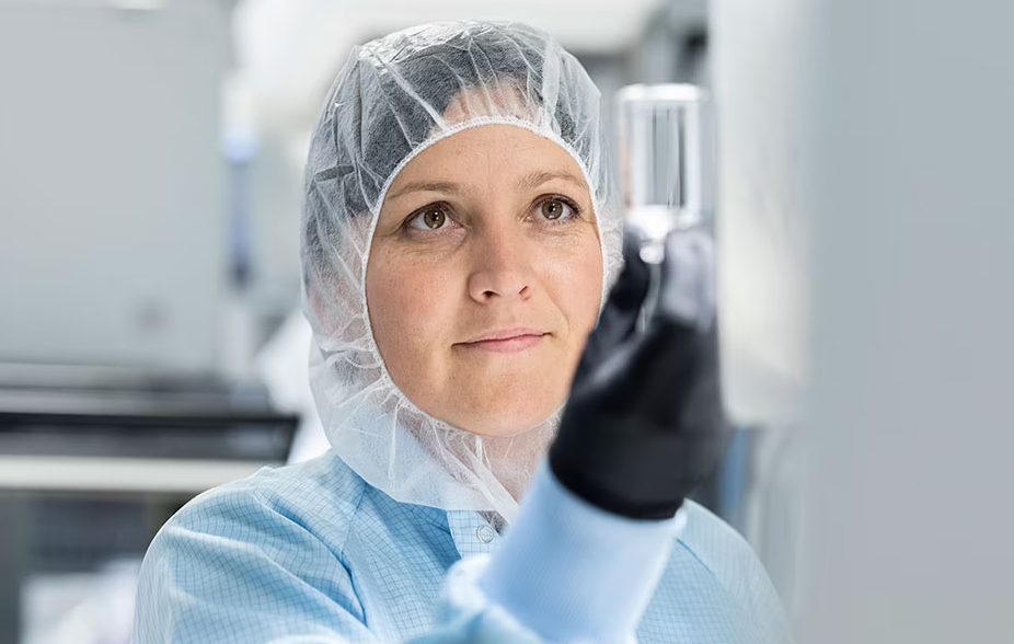 Una mujer que lleva exfoliantes médicos sostiene un contenedor de muestra para inspeccionar su contenido.