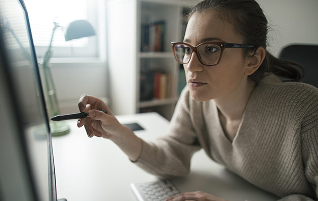 Mujer con gafas apuntando hacia el monitor de su ordenador con un bolígrafo