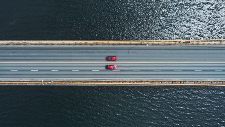 Deux voitures rouges roulent sur l'autoroute au-dessus de l'eau