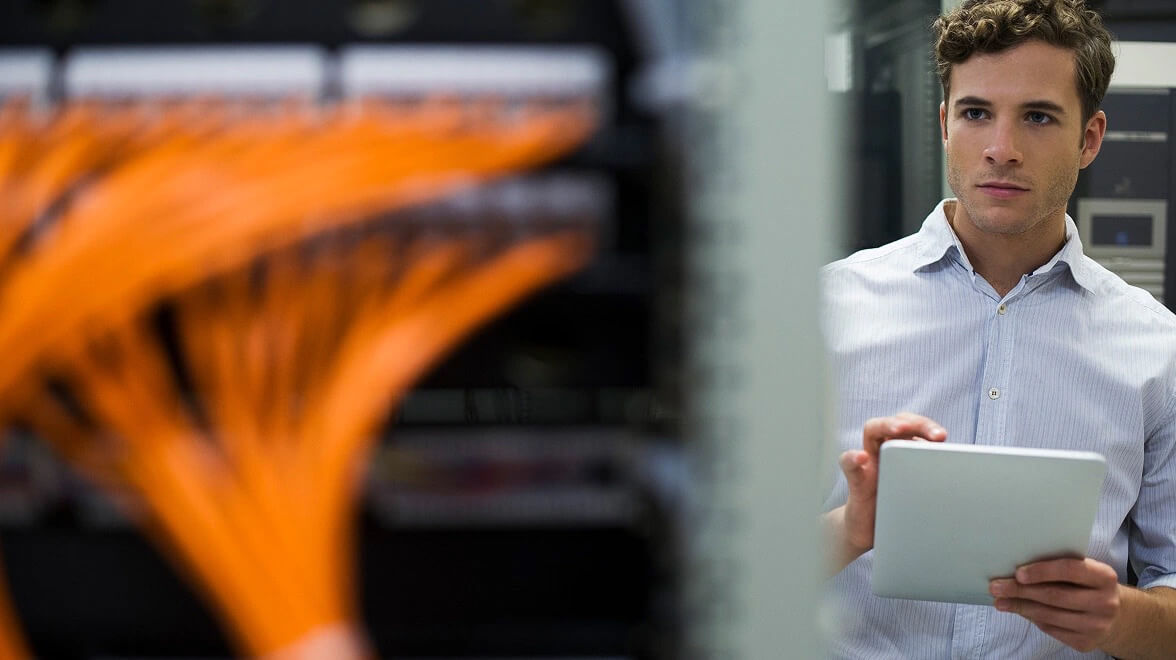 Un ingénieur examine l'infrastructure réseau et le câblage orange à l'aide d'une tablette numérique.