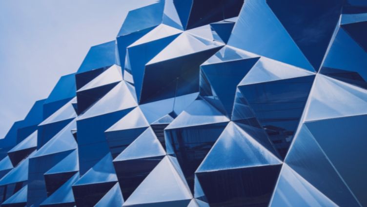 Vista ravvicinata della facciata di un edificio moderno con un motivo geometrico di pannelli angolari blu riflettenti.