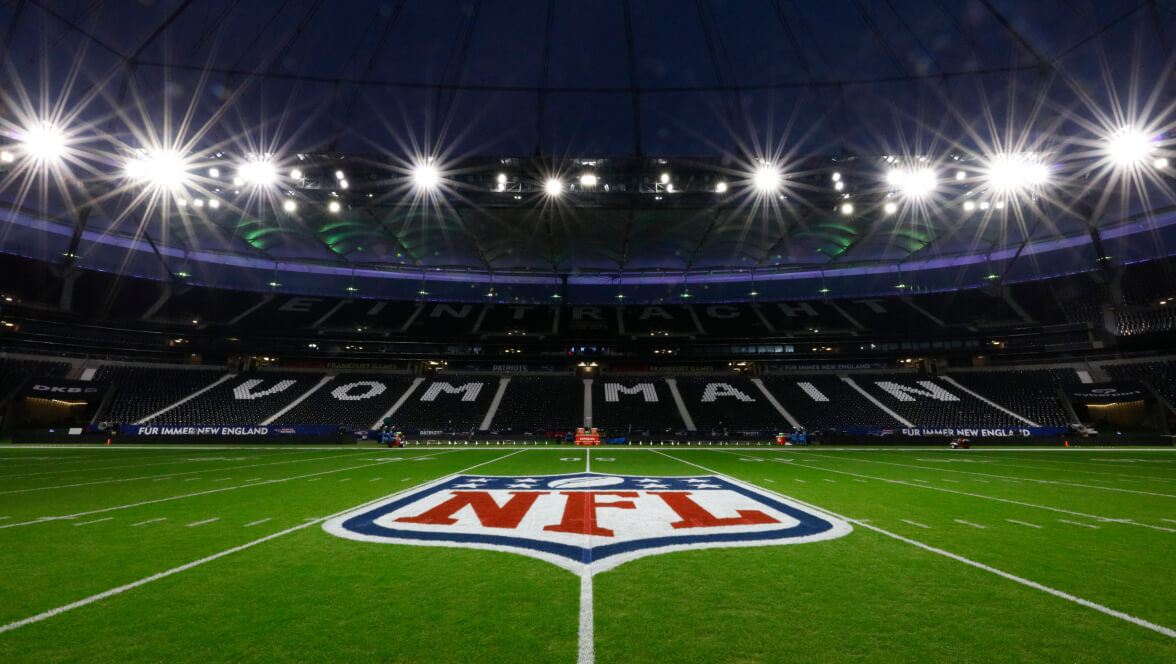 Campo della NFL di notte con il logo dello scudo della NFL a centrocampo all'interno di uno stadio illuminato.