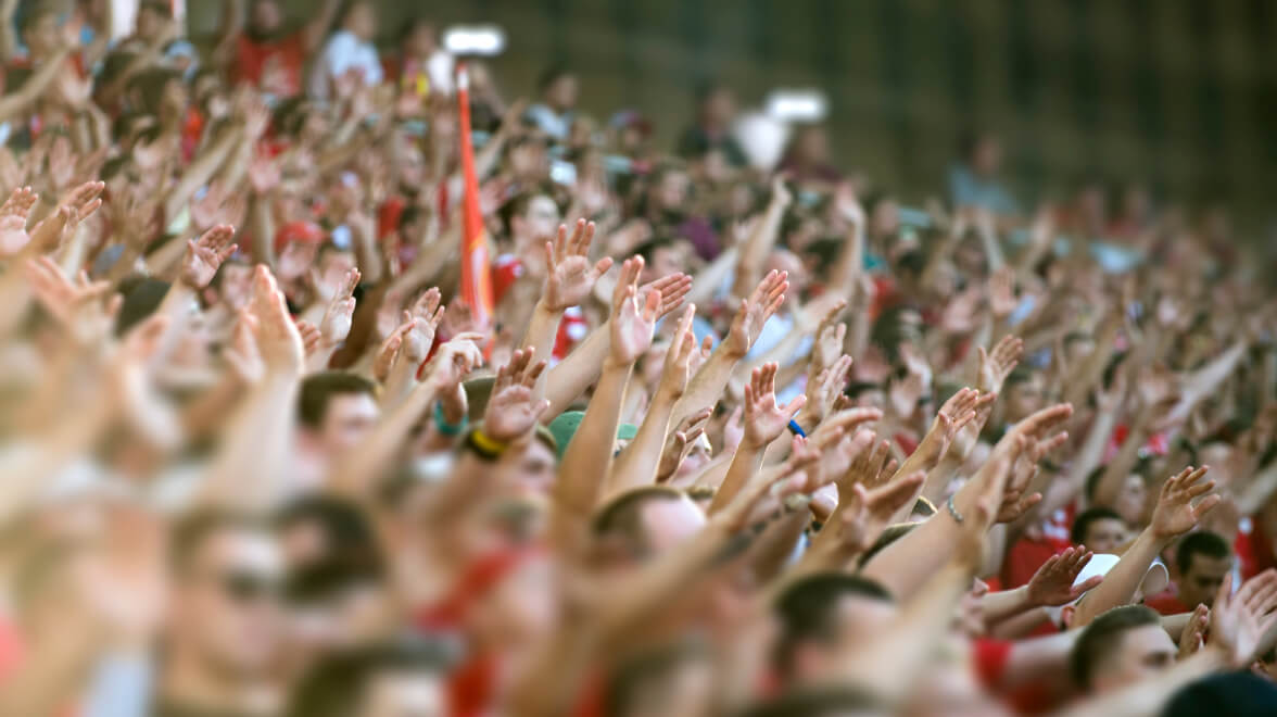Un'ampia folla di tifosi entusiasti alza le mani all'unisono durante un evento allo stadio.
