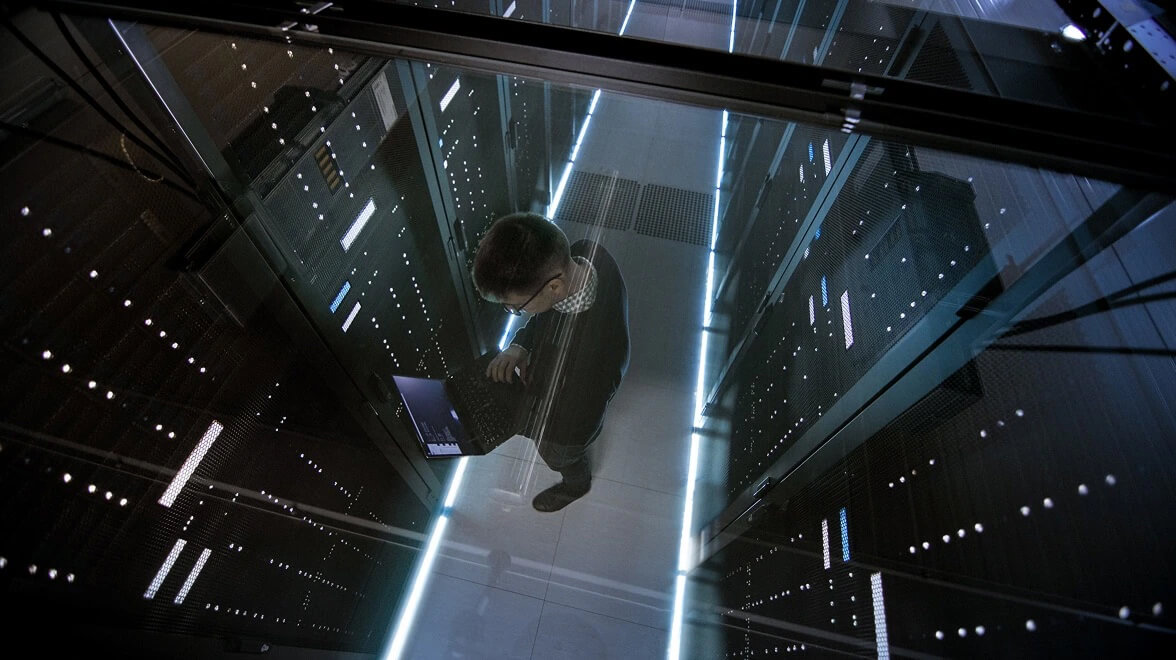 Specialista IT che lavora in un corridoio di un data center circondato da rack di server illuminati.