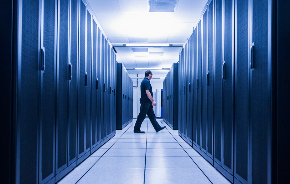 A man in a security outfit walking between the hardware aisles of a data security center.