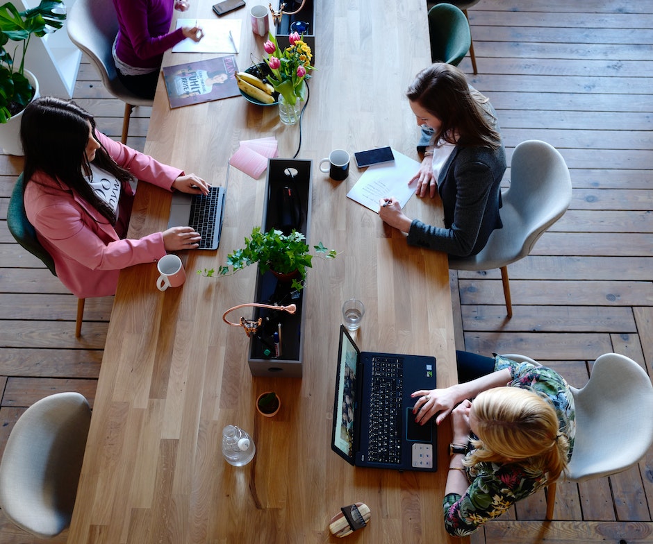 people sitting in front of their laptops on big wooden table working
