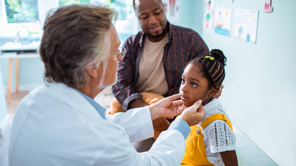 doctor examining the child while her father is sitting beside her on the patient table