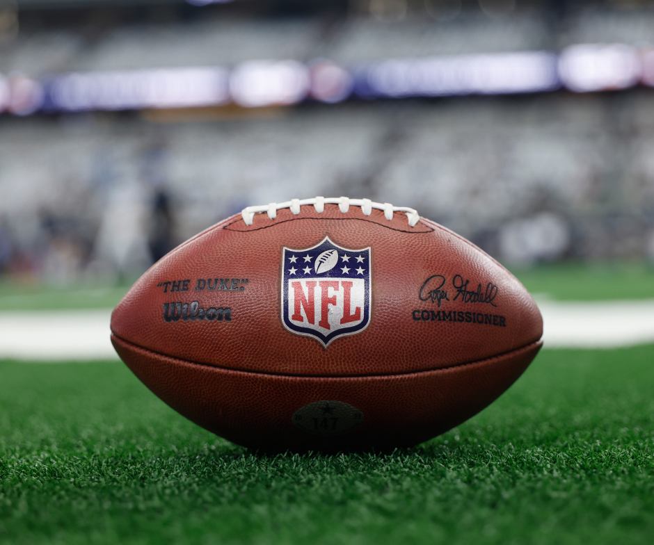Close‑up of an NFL football resting on the field with the NFL logo prominently displayed.