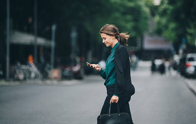 mulher olhando para o telefone ao atravessar a rua